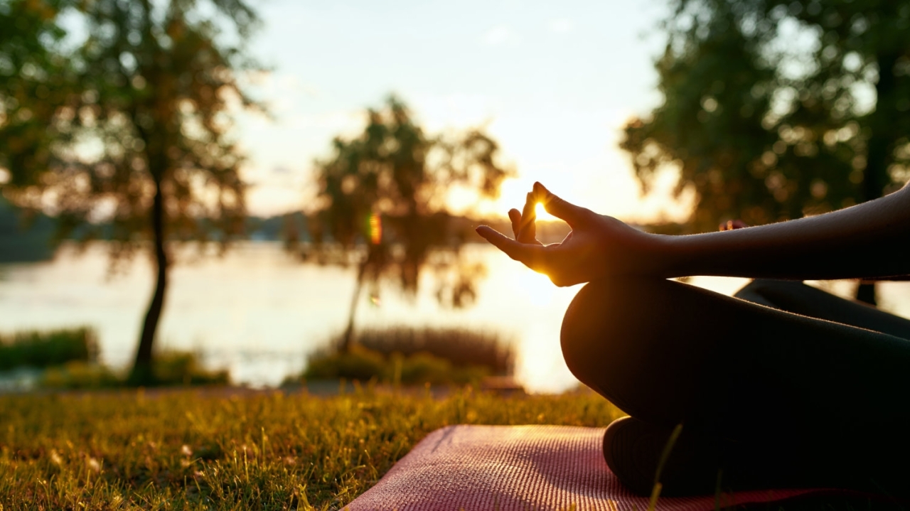 Cropped shot of a woman doing yoga outdoors near lake or river a - Mental and physical health. Cropped shot of a woman doing yoga outdoors near lake or river at sunrise in the morning, sitting in lotus pose on the background of nature. Meditation and yoga
